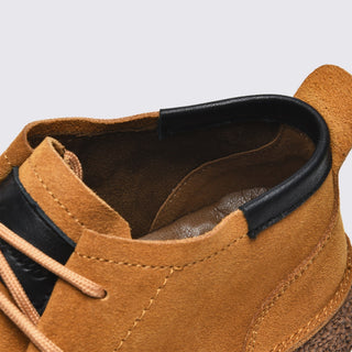 Close-up of a brown suede shoe with black interior lining on a light gray background