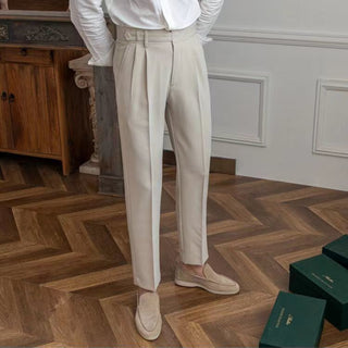 Person wearing beige pants and white shirt standing on a wooden floor with green boxes in the background.