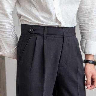 Person wearing a white shirt and dark pleated pants with a blurred background