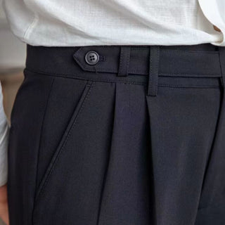 Close-up of dark pleated pants with a button, worn by a person.
