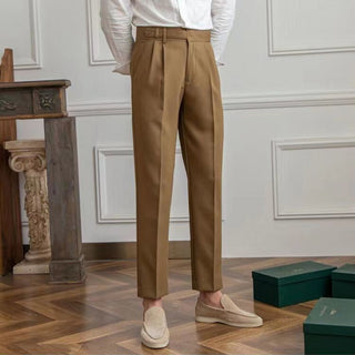 Person wearing brown trousers and white shirt in a room with wooden floor and decorative wall.