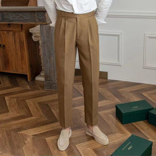 Person wearing brown pants and white shirt standing on a wooden floor with green boxes in the background.