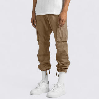 Person wearing brown cargo jogger pants and white sneakers on a plain background
