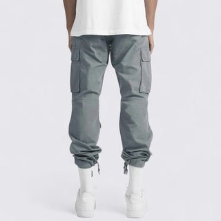 Person wearing gray cargo pants and white shoes on a white background