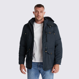 Man wearing a dark blue jacket over a white shirt and jeans on a light gray background