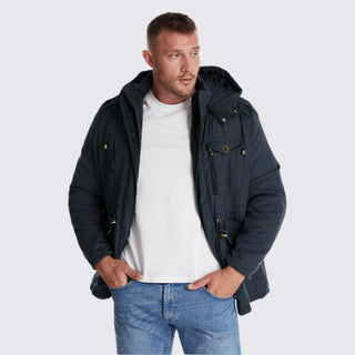 Man wearing a navy jacket over a white shirt and blue jeans on a light gray background