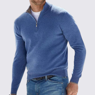 Man wearing a blue quarter-zip sweater and jeans on a light gray background