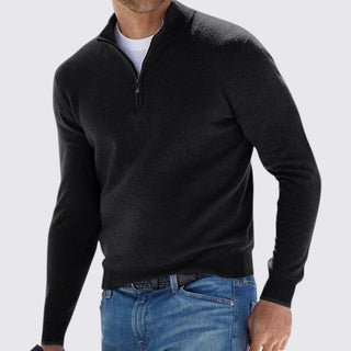 Man wearing a black quarter-zip sweater and blue jeans on a light gray background
