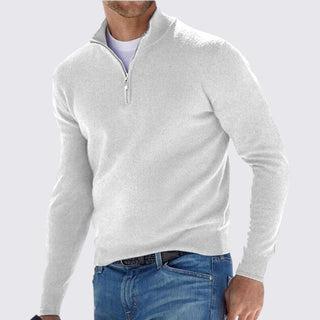 Man wearing a light gray quarter-zip sweater and blue jeans on a white background