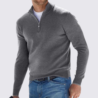 Man wearing a gray quarter-zip sweater and blue jeans on a light gray background