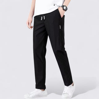 Person wearing black pants and white sneakers on a light gray background