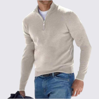 Man wearing a beige half-zip sweater and blue jeans on a light gray background