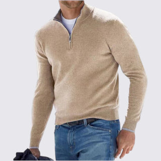 Man wearing a beige half-zip sweater and blue jeans on a light gray background